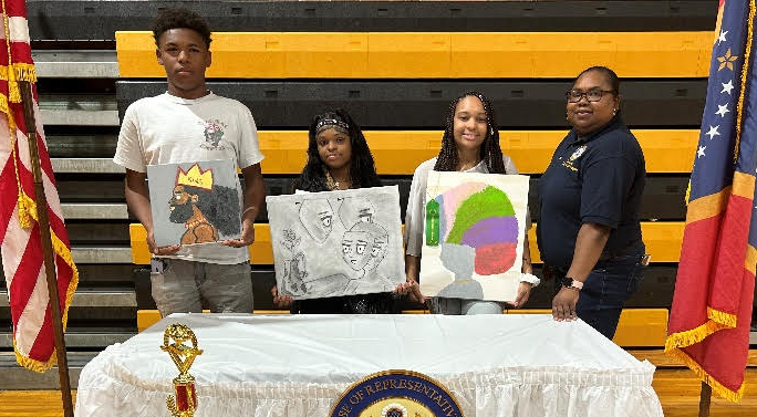 Three African American high school students and one adult pose between two the US and Mississippi State Flags holding their artwork