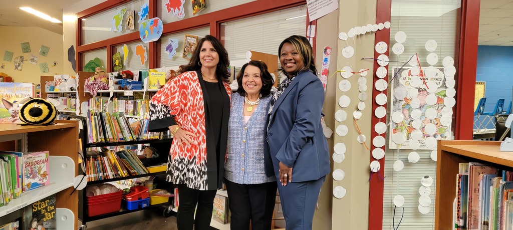 Principal Tammy Burris, Muriel Summers, and Principal Tawanda Nichols pose for the camera in the library at Sherman Avenue Elementary School. Colorful books are in shelves in the background. 